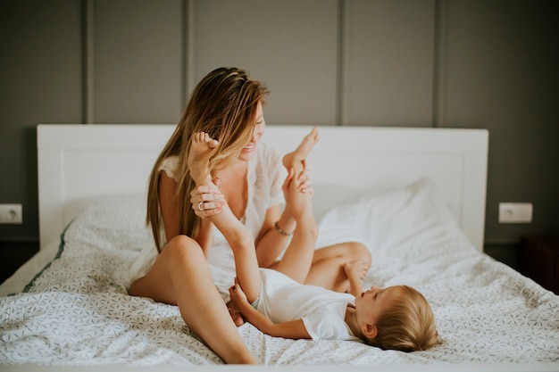 Photo young happy mother playing in a white bed enjoying a sunny morning in home bedroom