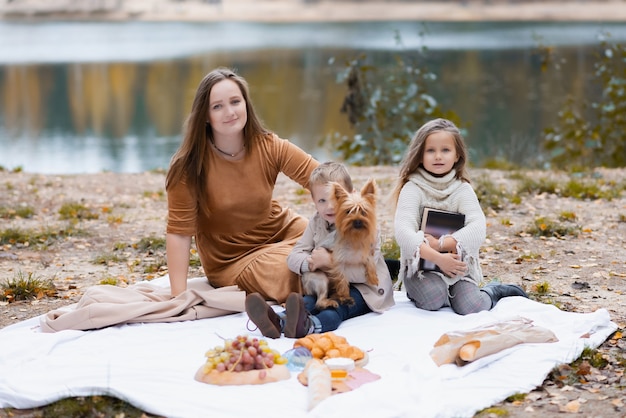 A young happy mother with two small children is having picnic in autumn park with colorful leaves