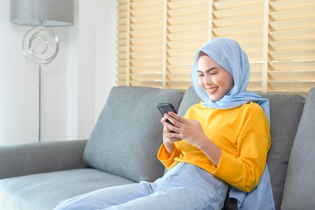 Young happy muslim woman relaxing and using smartphone in living room