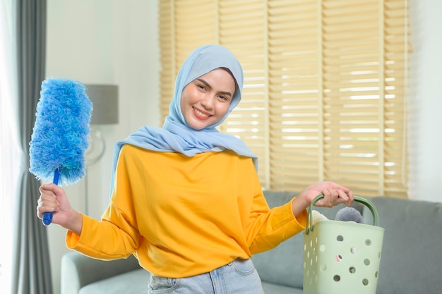 Young happy muslim woman wearing yellow gloves and holding a basket of cleaning