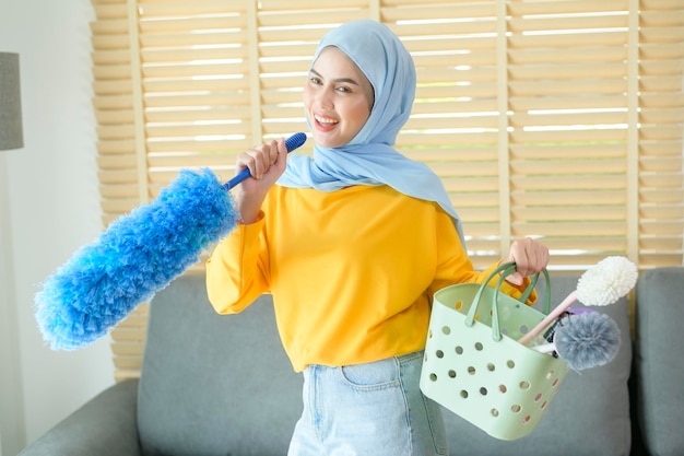 Young happy muslim woman wearing yellow gloves and holding a basket of cleaning