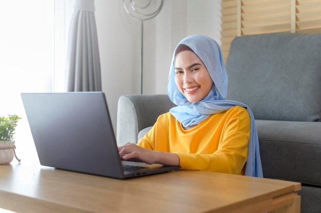 Young happy muslim woman working on laptop in living room at home