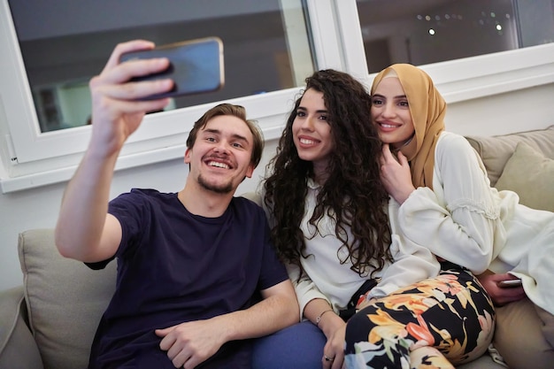 Young happy, muslims taking selfie in house. Man with two women spending time together