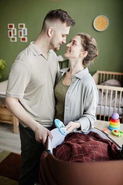 Young happy parents with newborn baby in cradle enjoying their parenthood at home