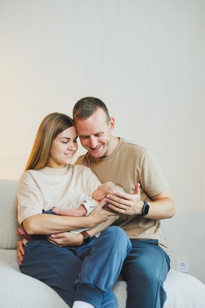 Young happy parents with a newborn baby in their arms at home on the couch Mom and dad with a newborn baby on a white background