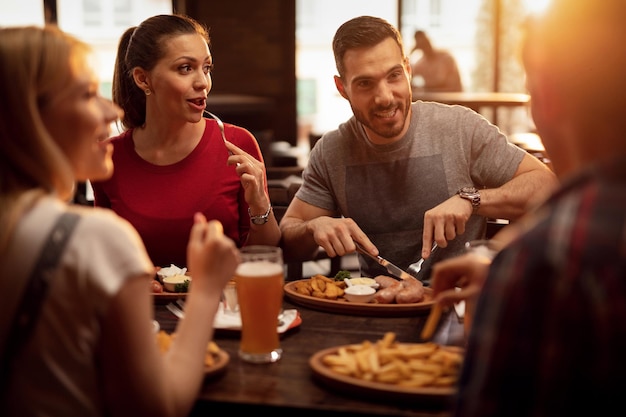 Young happy people eating in a pub and talking to each other