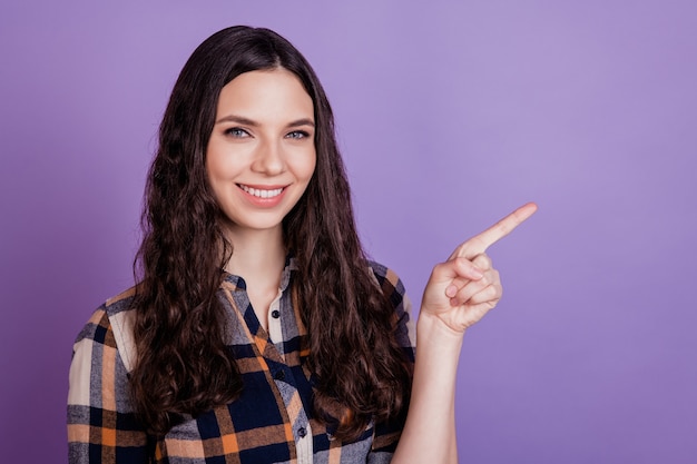 Young happy positive smiling woman suggest select advert point index finger empty space isolated on violet background