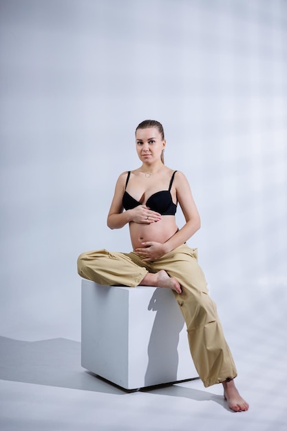 Foto giovane donna incinta felice in reggiseno e pantaloni su sfondo bianco gravidanza felice elegante donna incinta pone in studio