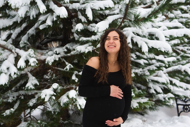 雪に覆われた森の若い幸せな妊娠中の女性