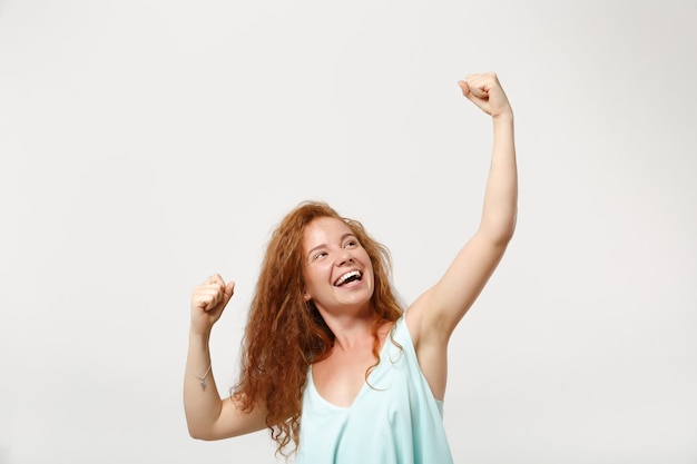 Young happy redhead woman girl in casual light clothes posing isolated on white background. People sincere emotions lifestyle concept. Mock up copy space. Clenching fists like winner, rising hands.