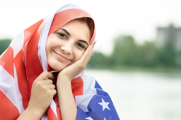 Young happy refugee woman with USA national flag on her head and shoulders
