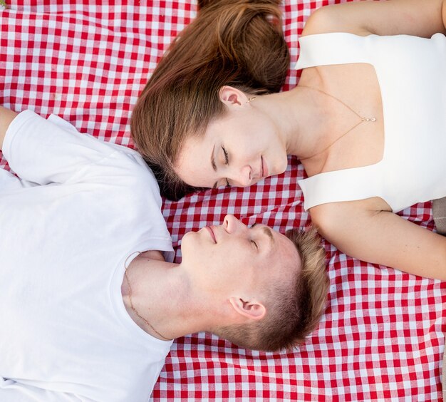 Young happy romantic couple cuddling on a picnic blanket looking to each other, top view