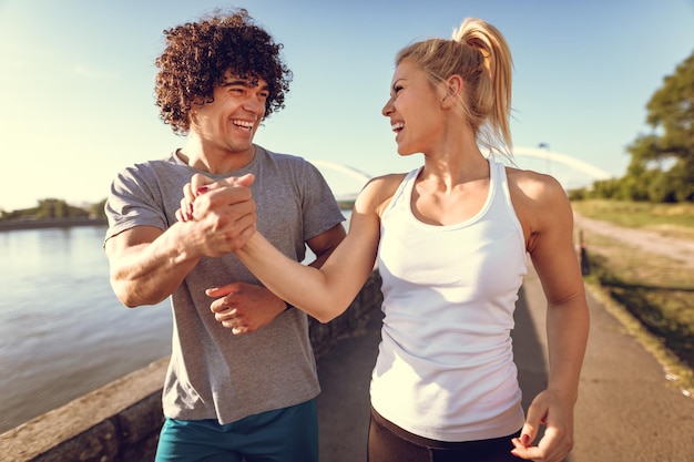 Young happy runners couple training outdoors by the river, working out in nature against blue sky with sunrise light.