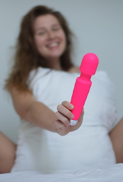 집에서 침실에서 침대에서 진동기로 자위하는 섹스 토이를 손에 들고 있는 젊은 행복한 섹시한 여성