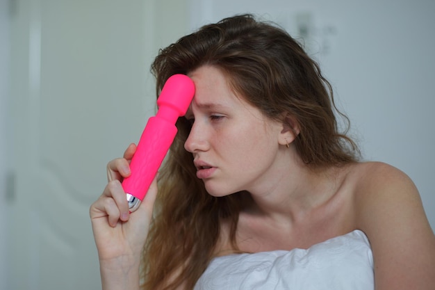 Молодая счастливая сексуальная женщина держит в руках секс-игрушку и мастурбирует вибратором в постели в спальне дома