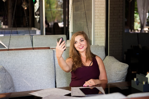 Young happy smiling beautiful plus size model making selfie, xxl woman in a cafe.