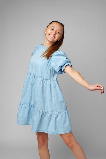 Young happy smiling woman in a light blue dress on a gray background