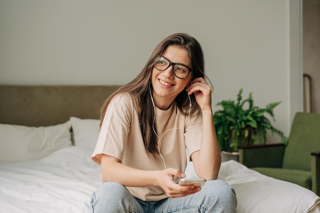young happy smiling woman sitting at home listening to music on phone headphones