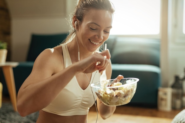 自宅でのトレーニング後に健康的なサラダを食べる若い幸せなスポーツウーマン