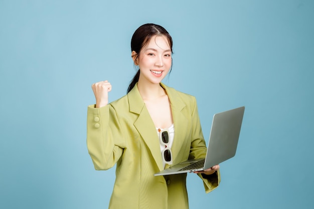 Young happy successful employee business woman 20s in casual green fashion jacket with laptop doing winner gesture isolated on pastel blue background Female entrepreneurs or office worker concept