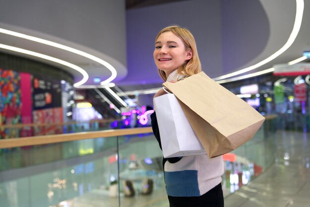 Young happy teenager girl shopping in mall with bags in hand