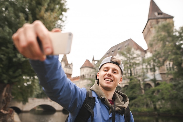 Young happy tourist takes selfie on historic buildings and a lake and smiling