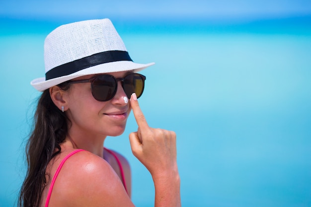 Молодая счастливая женщина, применяя лосьон для загара на носу на белом пляже