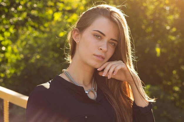 Young happy woman in black blouse touching her long hair on the background of green trees