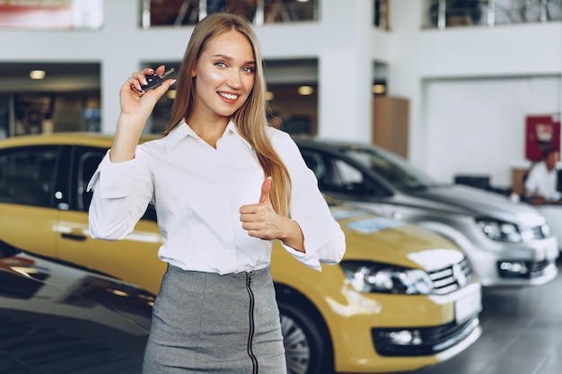 手に鍵を持って車の近くの若い幸せな女性の買い手/売り手