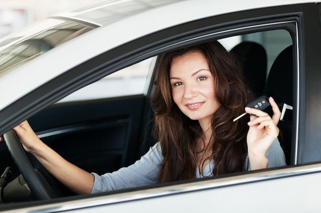 Young happy woman in car with keys smiling - concept of buying car