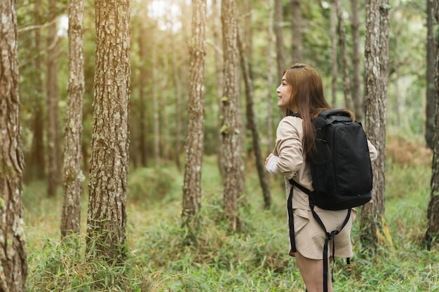 バックパック旅行を運び、森の中を歩く若い幸せな女性