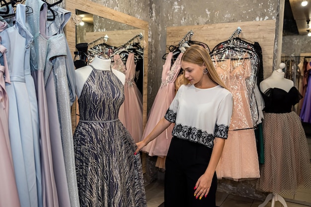 Young happy woman choosing and trying on dress clothes during shopping in boutique stylish lifestyle