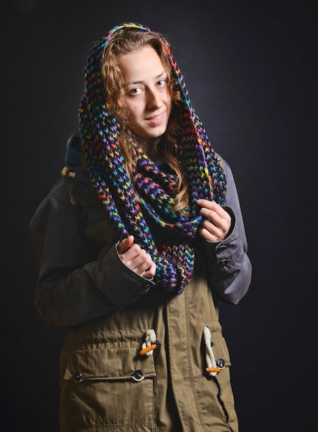Young happy woman in coat park and scarf on head in studio on a black background