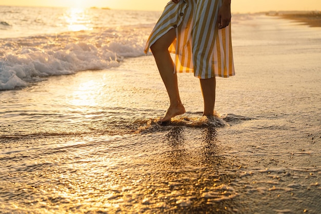 Молодая счастливая женщина танцует, кружась у моря в желтом развевающемся платье Морской пейзаж на рассвете с красивым небом Девушка смотрит на волшебный восход