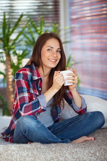 自宅のソファでコーヒーを飲む若い幸せな女性