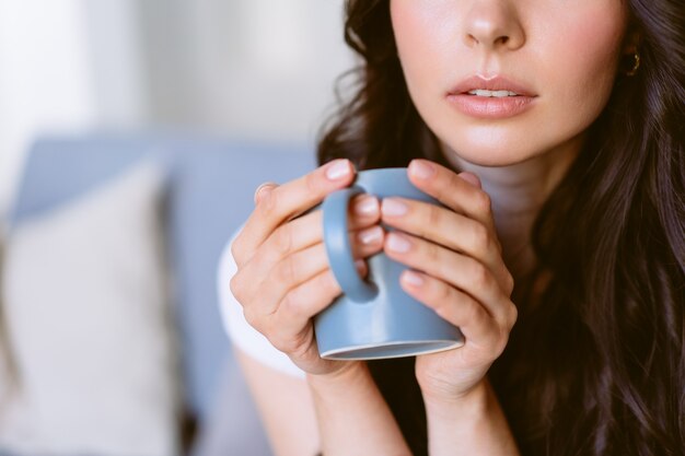 お茶を飲み、明るいアパートのソファに座って夢を見ている若い幸せな女性。