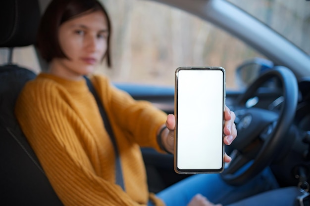 A young happy woman driving a car she shows empty phone screen