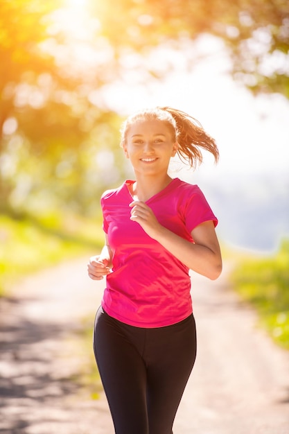 молодая счастливая женщина наслаждается здоровым образом жизни во время пробежки по проселочной дороге через красивый солнечный лес, упражнения и фитнес-концепцию