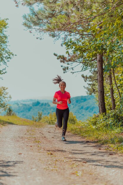 Young happy woman enjoying in a healthy lifestyle while jogging on a country road through the beautiful sunny forest, exercise and fitness concept.