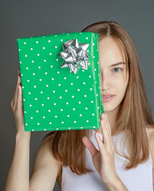 Young happy woman giving gift box to camera with excited smile greeting on holiday and sharing present