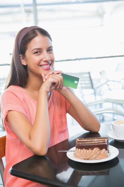 Young happy woman holding credit card and a cake in front of her in the cafe