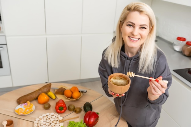 Young Happy Woman holding honey Enjoying While cooking healthy food In Kitchen. Detox Diet, Weight Loss Nutrition Concept.