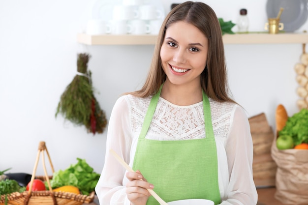若い幸せな女性は、キッチンで新鮮なサラダを調理または食べています。食品と健康の概念。
