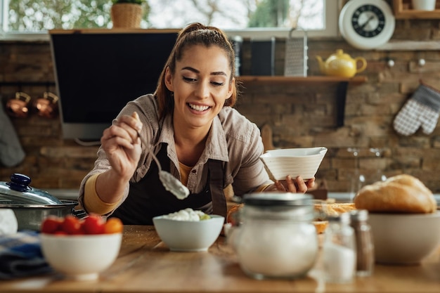 Giovane donna felice che prepara salsa di immersione durante la cottura in cucina