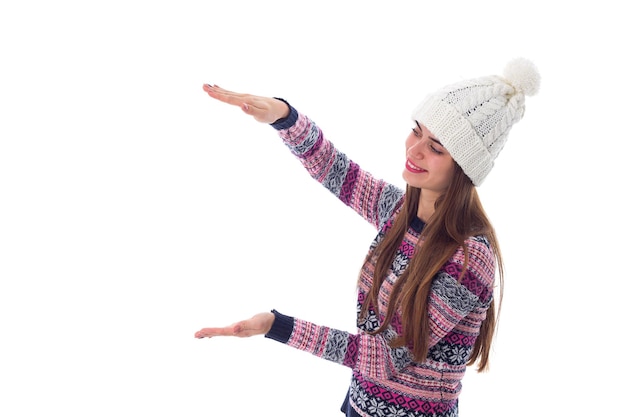 Young happy woman in purple sweater and white hat holding something on white background in studio