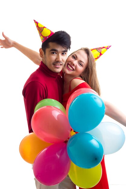 Young happy woman in red dress with colored hat and handsome man in red shirt blowing balloons