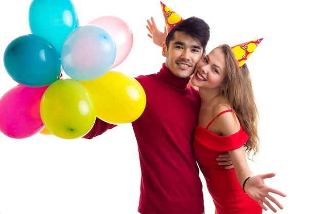 Young happy woman in red dress with colored hat and handsome man in red shirt blowing balloons