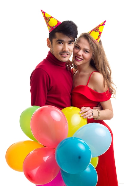 Young happy woman in red dress with colored hat and handsome man in red shirt blowing balloons