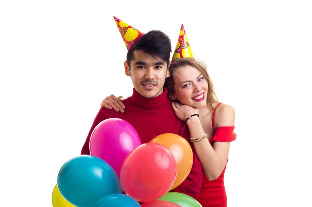 Young happy woman in red dress with colored hat and handsome man in red shirt blowing balloons