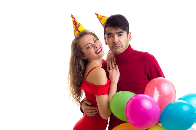 Young happy woman in red dress with colored hat and handsome man in red shirt blowing balloons